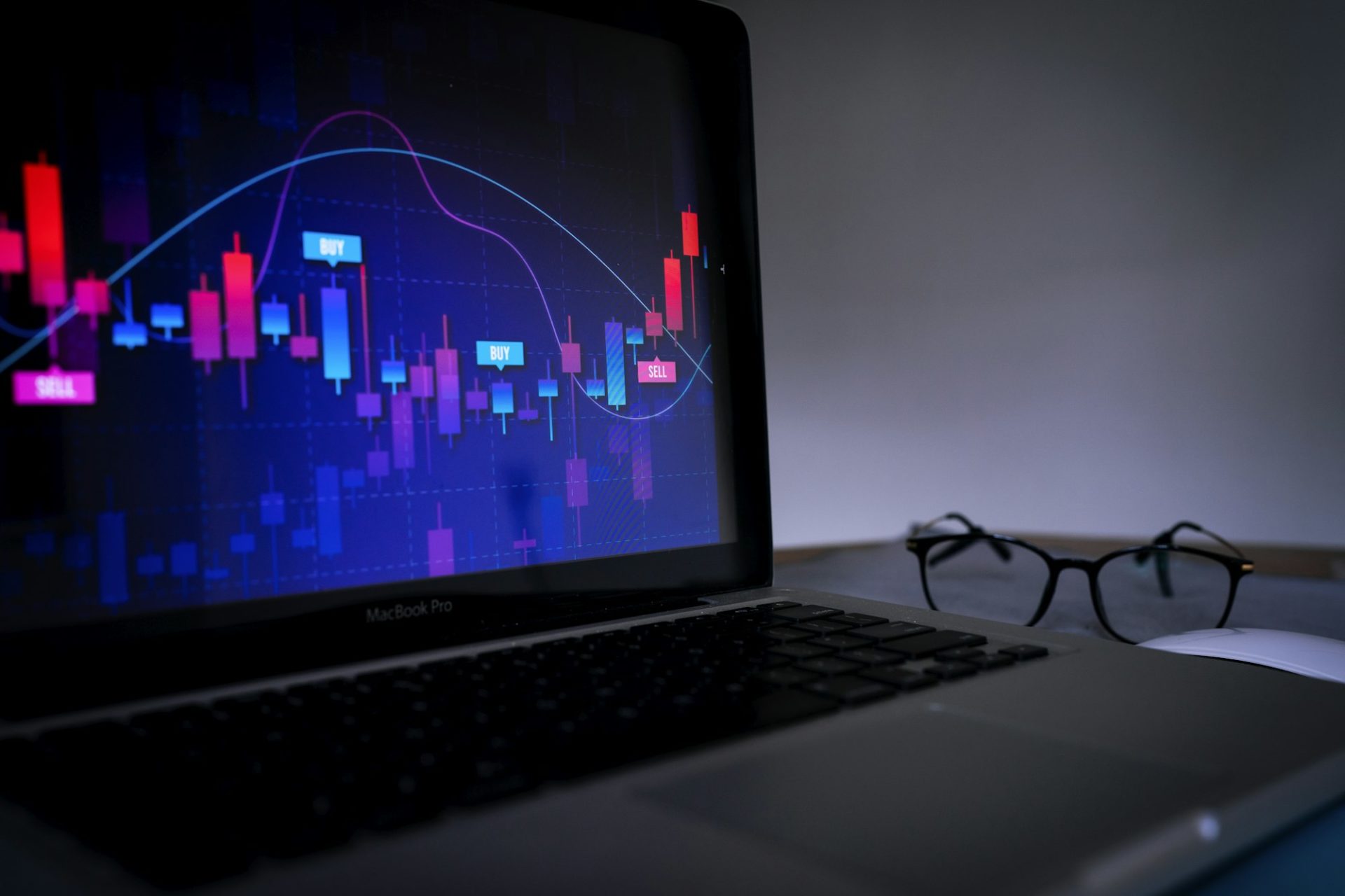 Laptop displaying a trading graph with glasses on the table